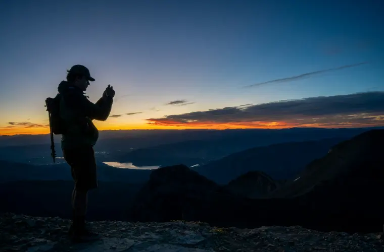 A hiker standing on a mountain summit at first light.