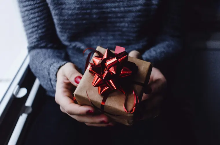 Someone holding a wrapped present with a red bow.