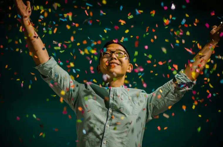 A person cheering under a shower of colourful confetti.