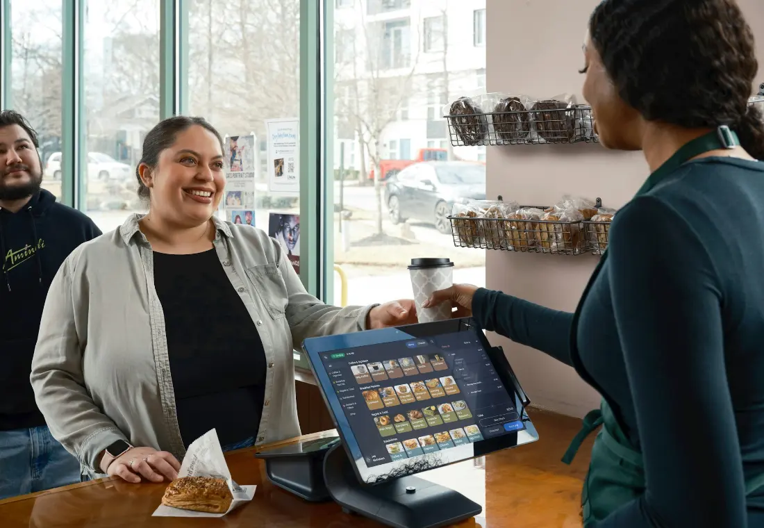 A barista handing a coffee across the counter to a smiling customer.