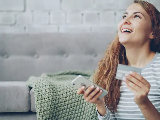A woman smiling as she holds a card and her phone.